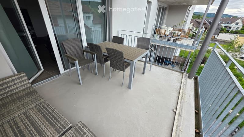 Balcony / Terrace. Balcony with a small table and four chairs, overlooking a residential area with other buildings and greenery.