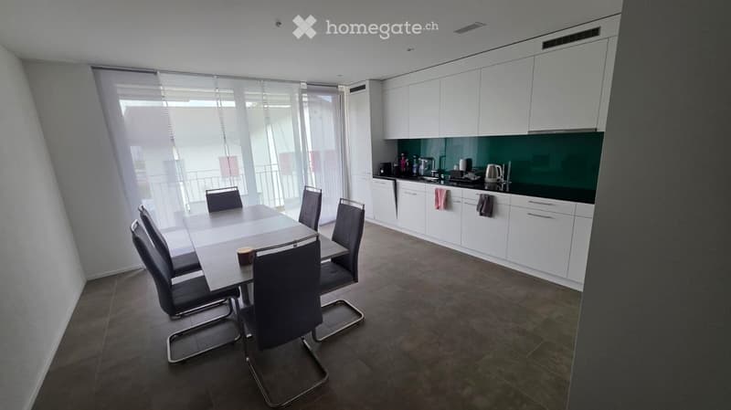Furnished Room. Modern kitchen and dining area with white cabinets, a dark green backsplash, a dining table with six chairs, and various kitchen appliances.
