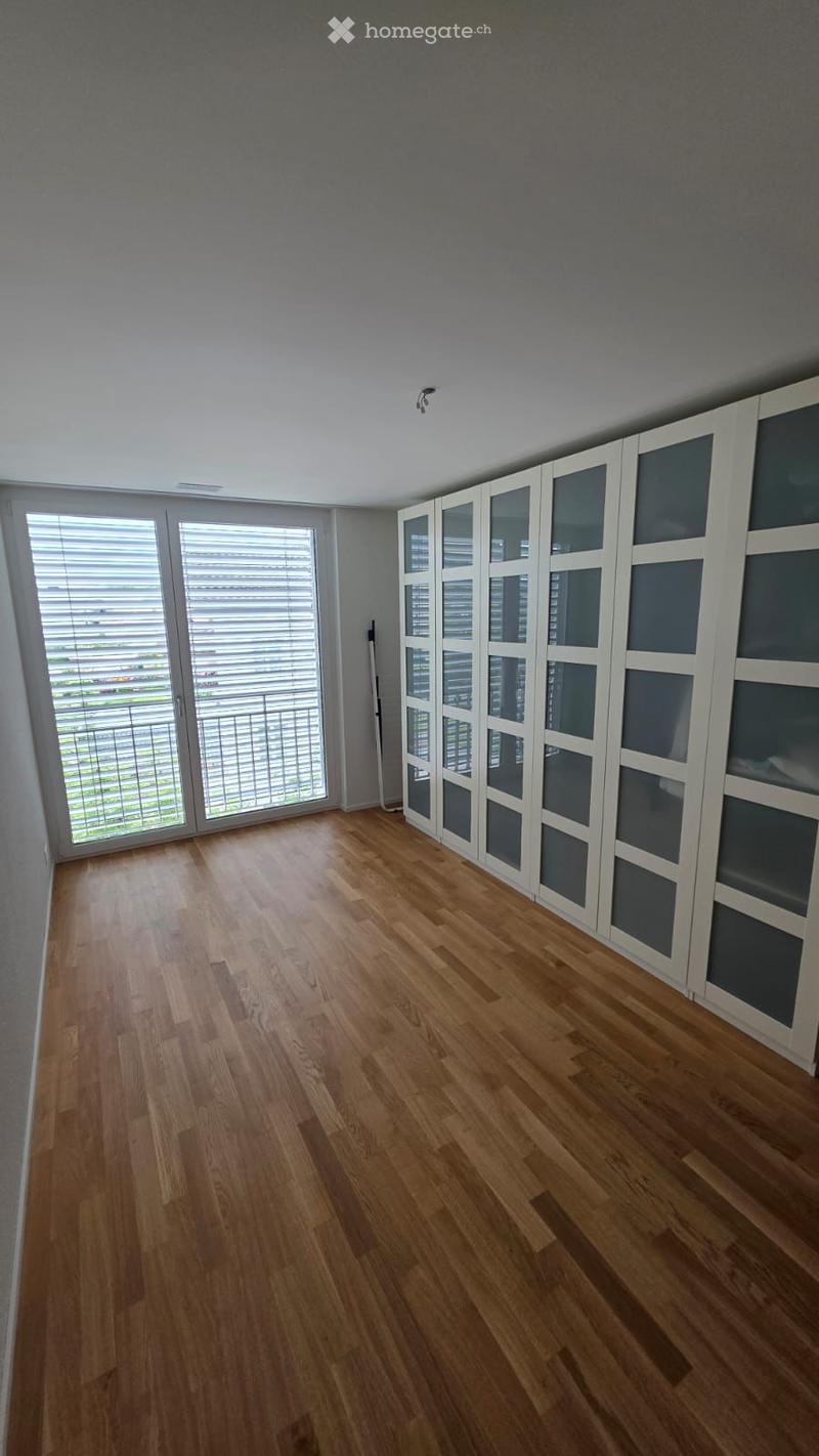 Unfurnished Room. Empty room with wooden flooring, white built-in closet with glass doors, large windows with blinds, and a view of a balcony area.