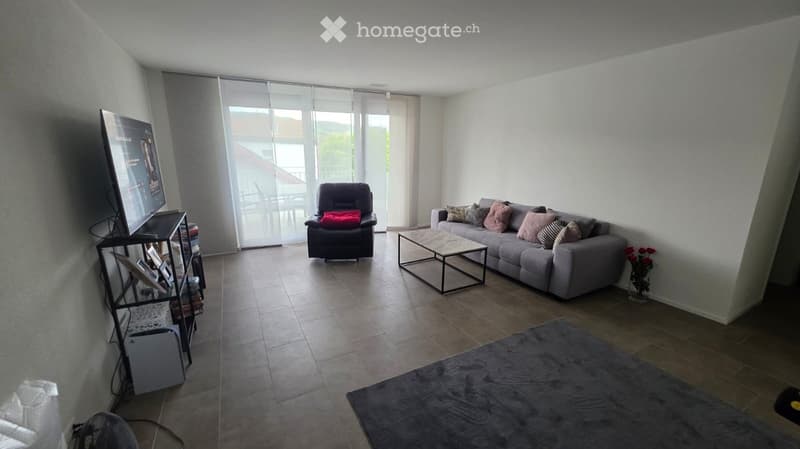 Living Room. Modern living room with large windows offering a view, grey sofa, coffee table, armchair, TV stand, and a rug.