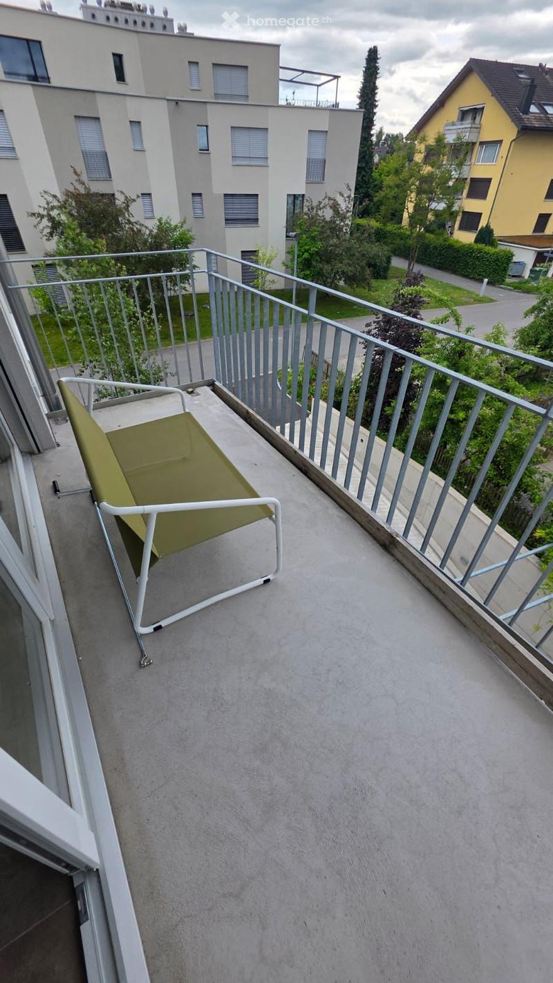 Balcony / Terrace. Balcony with a green folding chair, metal railing, and a view of surrounding buildings and greenery.