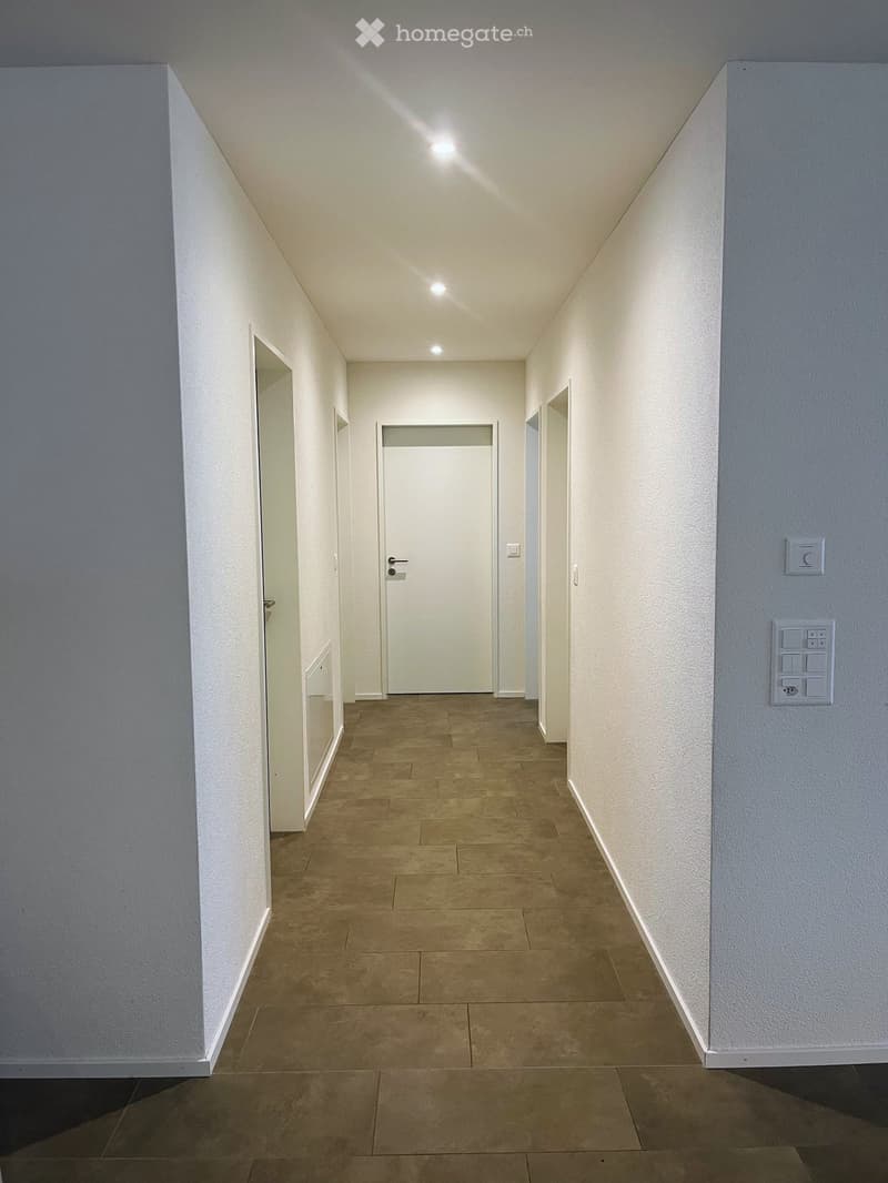 Empty hallway with tiled flooring, white walls, and overhead lighting.