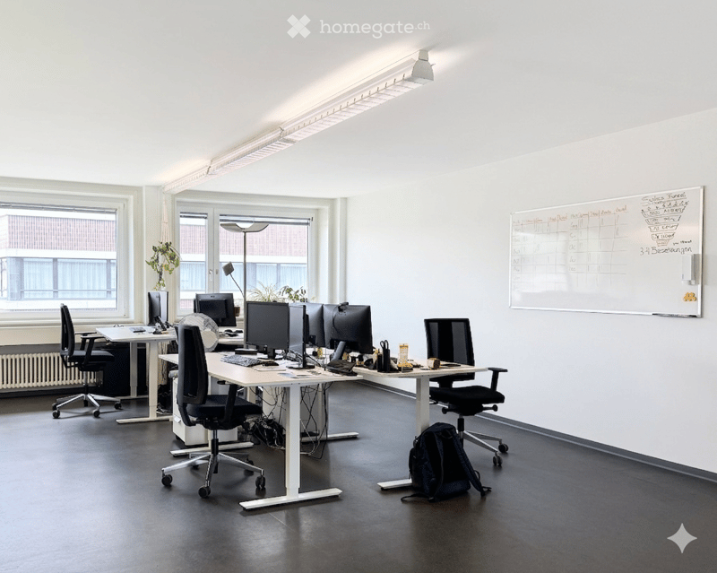Furnished Room. Modern office space with desks, chairs, multiple computer monitors, laptops, a whiteboard, and a small plant near the window.