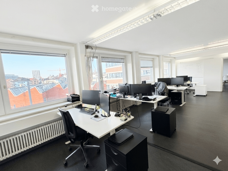 Furnished Room. Modern office space with multiple desks, chairs, computer monitors, keyboards, mice, printers, and cabinets. Large windows offer a city view.