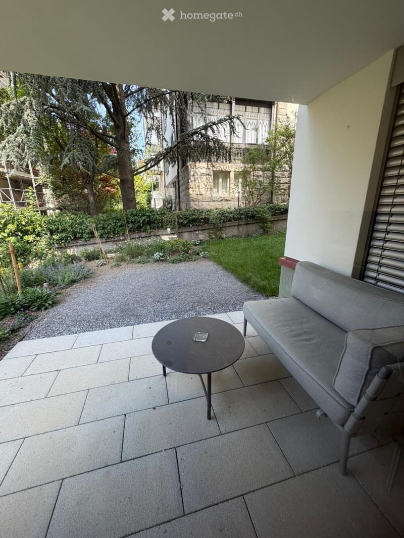 Balcony / Terrace. Balcony with a grey sofa, a round table, and a view of a garden and trees.