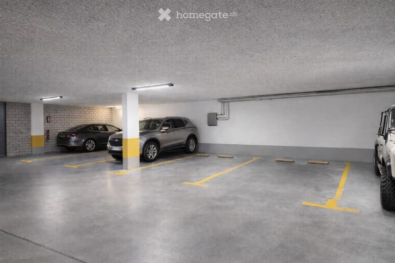 Building. Underground parking area with several parked cars, marked parking spaces, and a central support column.