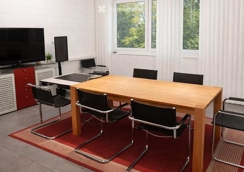 Furnished Room. A modern office or meeting room with a large wooden table, several black chairs, a TV screen, and a smaller screen on a cabinet.
