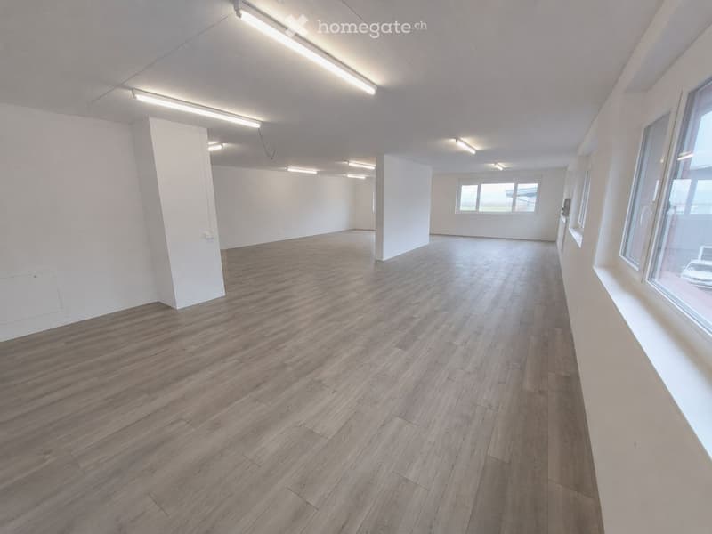 Empty room with wooden flooring, white walls, and large windows allowing natural light. No furniture or equipment is present.