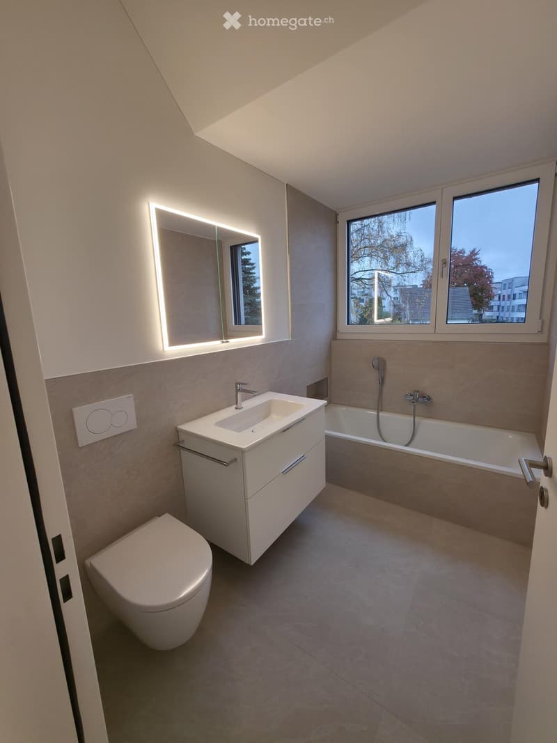 Bathroom. Modern bathroom with a toilet, sink, bathtub, and illuminated mirror. The space features large windows and sleek, contemporary design elements.