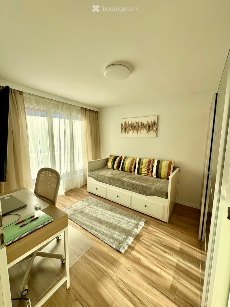 A room with a desk, chair, daybed, rug, and a painting on the wall.