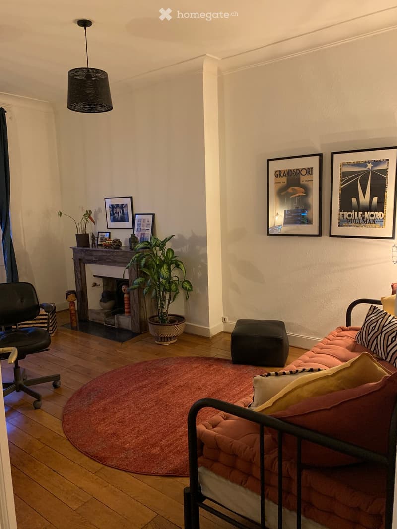 Furnished Room. A cozy living space with a pink sofa, a black office chair, a small table with a plant, and several picture frames on the wall.