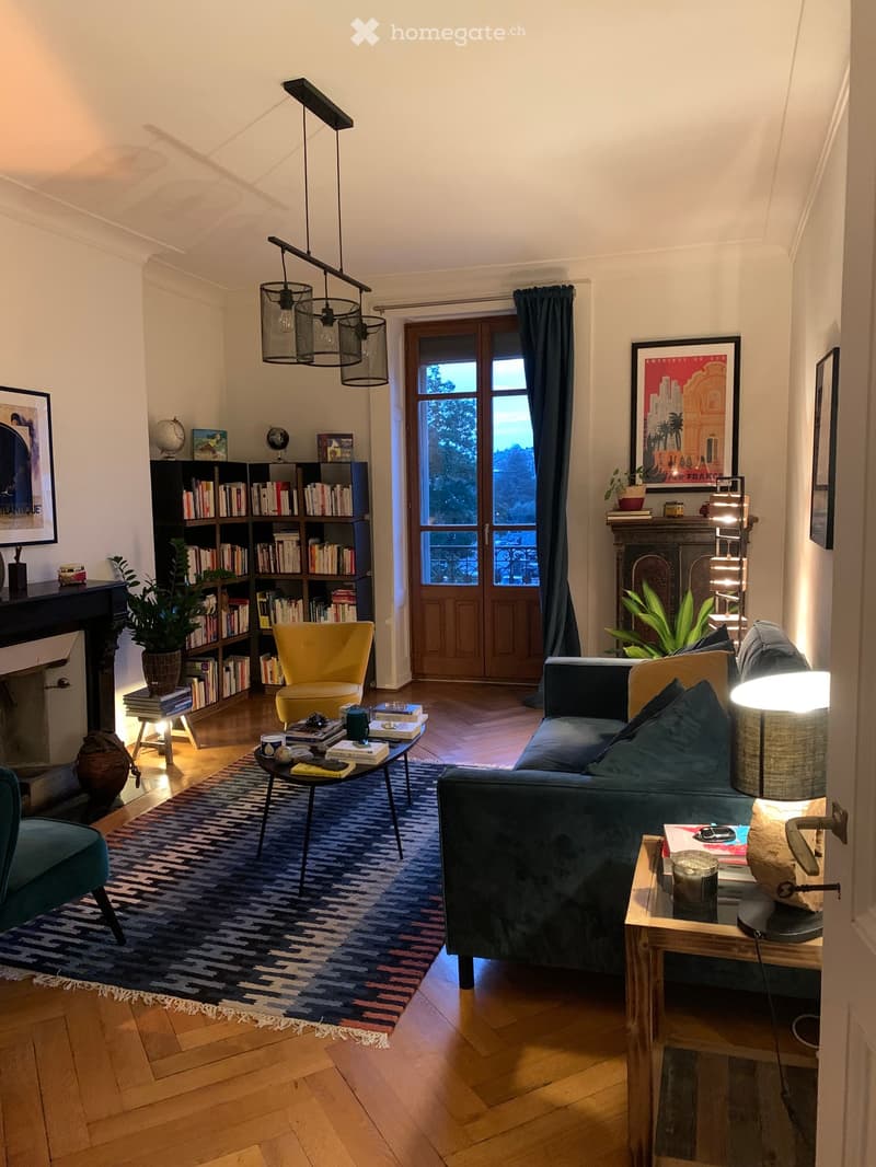 Living Room. Modern living room with wooden flooring, a patterned rug, a blue sofa, a yellow armchair, a coffee table, side tables, a bookshelf, and a fireplace.