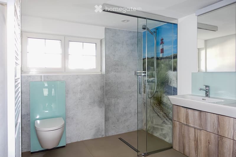 Bathroom. Modern bathroom with a glass-enclosed shower, a toilet with a light blue panel, a wooden vanity with a sink, and a large mirror above the sink. The shower features a scenic mural of a lighthouse and beach.