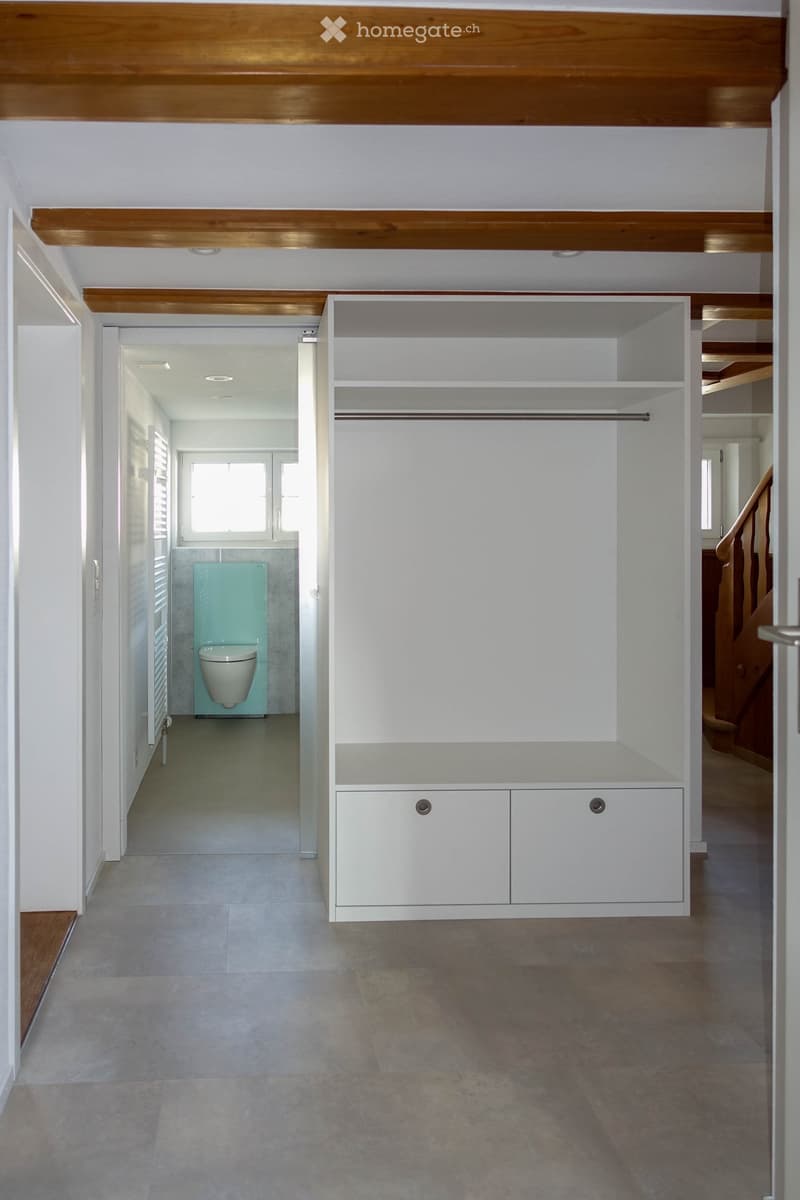 Corridor / Hallway. Modern hallway with white walls, wooden ceiling beams, built-in storage unit, and a small bathroom visible at the end.