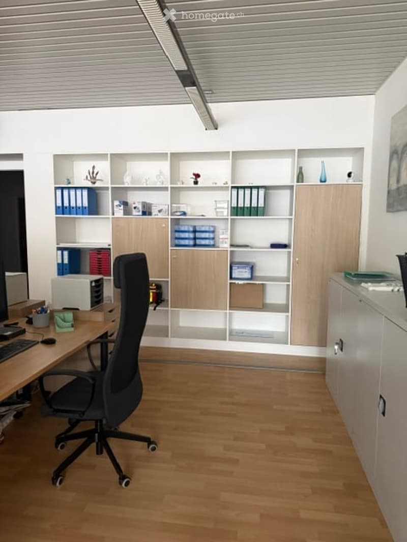 Furnished Room. Modern office space with light wood flooring, white walls, built-in shelving units, a black office chair, a wooden desk with a computer, keyboard, and mouse, and decorative vases on the shelves.