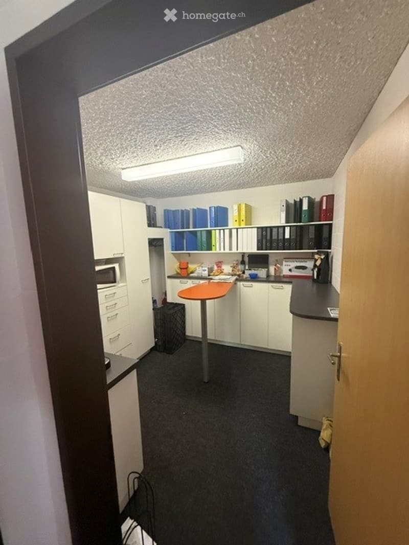 Furnished Room. A small, furnished room with a round orange table, white cabinets, a microwave, shelves with binders, and a filing cabinet.