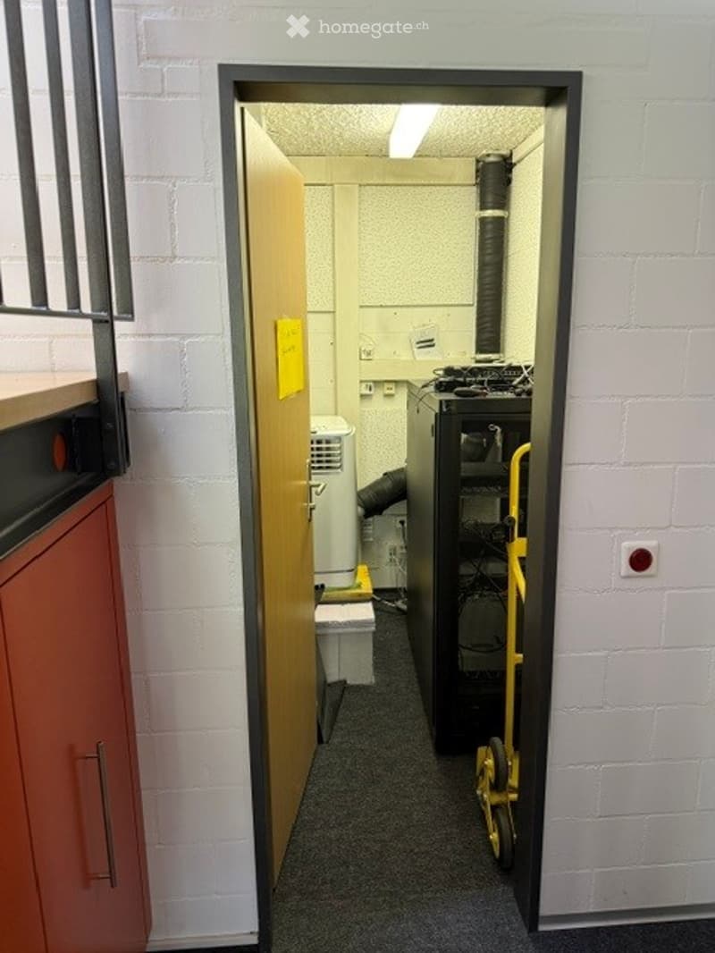Corridor / Hallway. A narrow hallway with white brick walls, a partially open door leading to a utility area, and visible equipment including a white air conditioner and a black server rack.