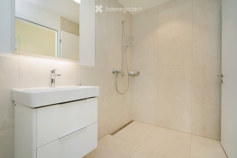 Bathroom. Modern bathroom with a white sink, mirror, and shower hose. Light beige tiles on walls and floor.