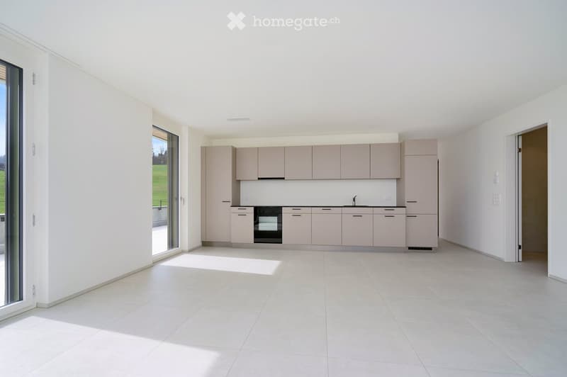 Kitchen. Modern, minimalist kitchen with light grey cabinets, a built-in oven, and white tiled flooring. Large windows provide natural light and a view of the outdoor area.