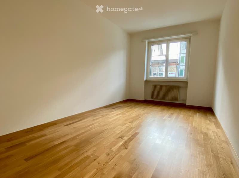 Unfurnished Room. Empty room with wooden flooring and white walls, featuring a single window with a radiator below it.