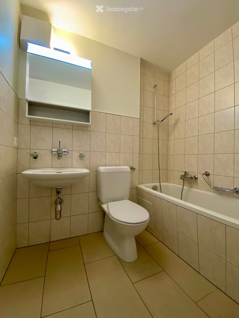 Bathroom. Modern bathroom with beige tiles, a sink, toilet, bathtub, and a built-in shelf above the sink.