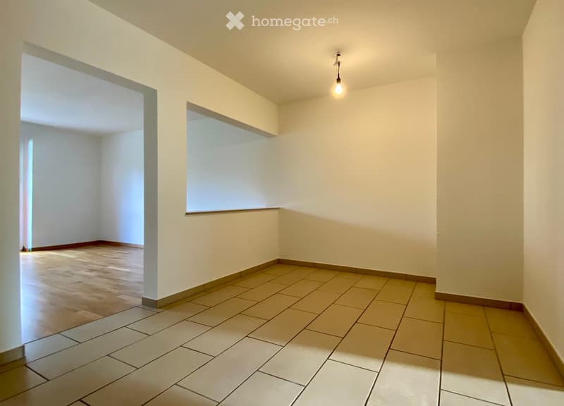 Unfurnished Room. Empty room with tiled floor and white walls, featuring a single hanging light fixture and an open doorway leading to another space.