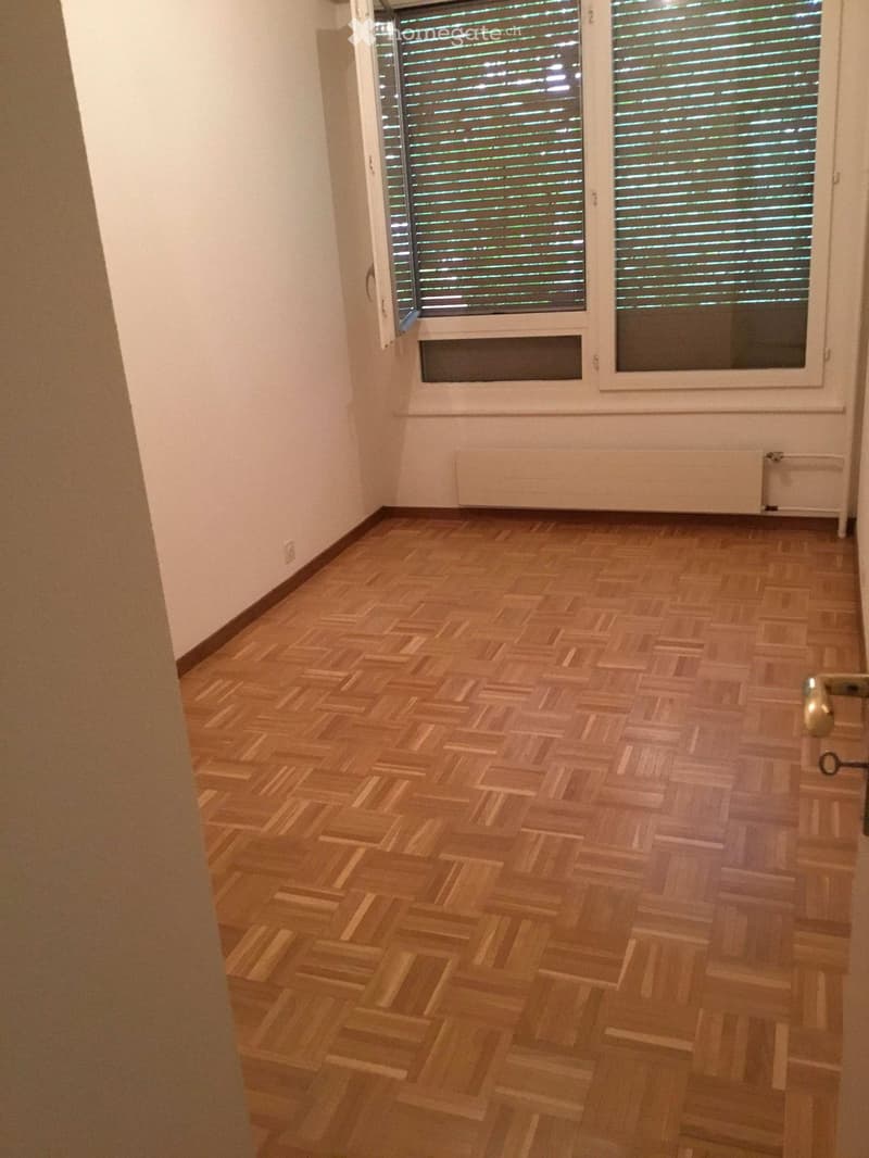 Unfurnished Room. Empty room with wooden parquet flooring, white walls, and a large window with blinds. No furniture or equipment is present.