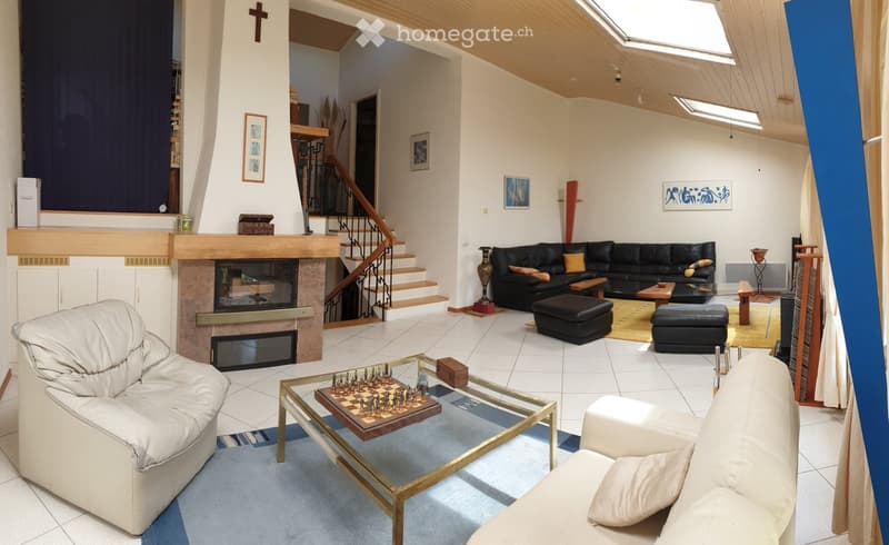 Living room with a fireplace, white tiled floor, and a mix of seating including a black leather sofa, white leather chairs, and ottomans. A glass coffee table with a chessboard is in the foreground.