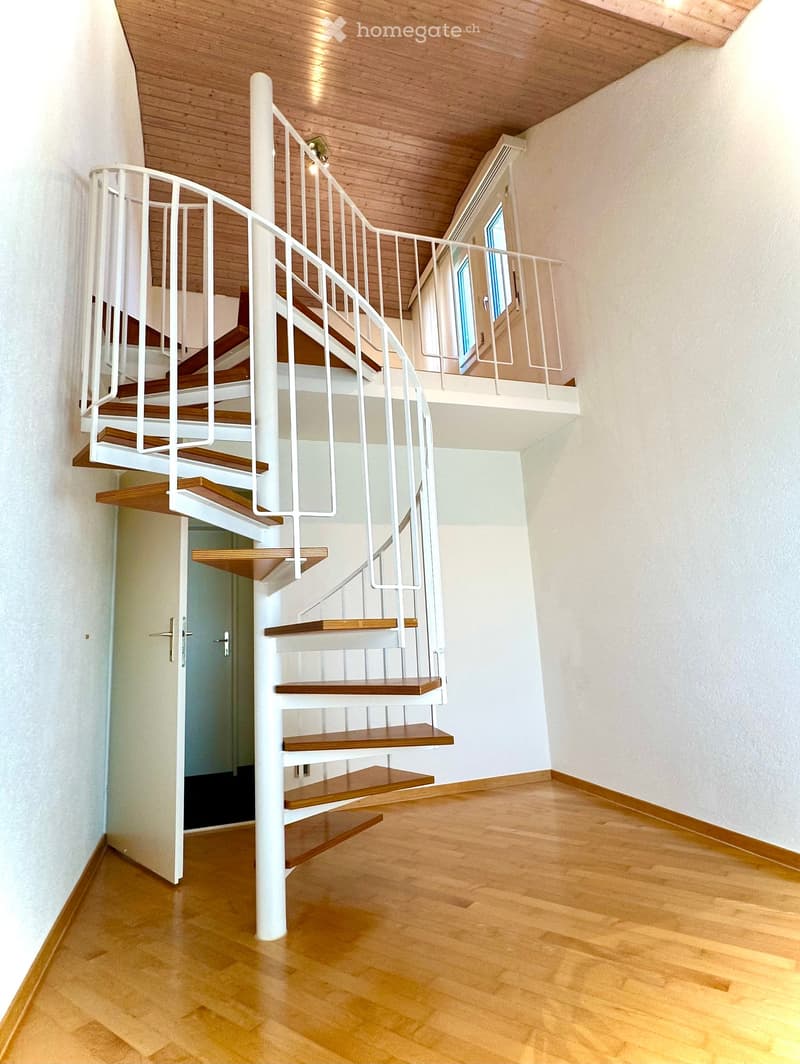 Corridor / Hallway. Spiral staircase with wooden steps and white railings, leading to an upper level with a window and balcony railing.