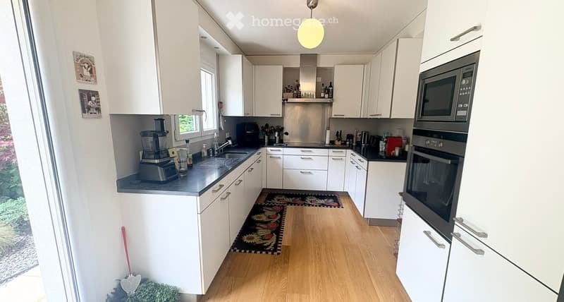 Kitchen. Modern kitchen with white cabinets, dark countertops, and wooden flooring. Features include a microwave, oven, blender, and various kitchen utensils.