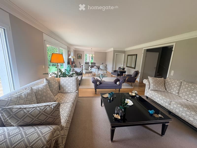 Living Room. Spacious living room with large windows, patterned sofas, coffee table, and additional seating area with chairs and a small table.