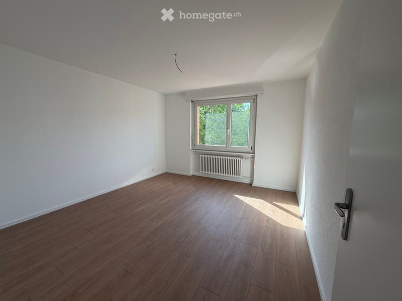 Empty room with wooden flooring, white walls, and a window with a radiator below it.