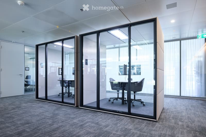 Modern office space with glass partitions, ergonomic chairs, and a small table in the foreground.