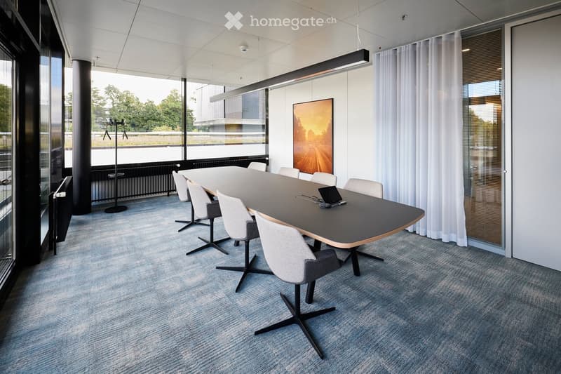 Modern conference room with a long, dark wooden table surrounded by white chairs, a laptop on the table, large windows with white curtains, and a painting on the wall.