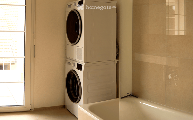 Bathroom. Bathroom with a bathtub, a stacked washing machine and dryer, and a large window letting in natural light.