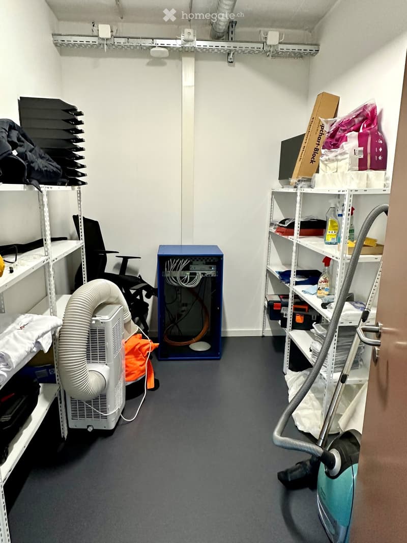 Furnished Room. A small, organized storage or utility room with shelves holding various items, a server rack, an air conditioner, and a vacuum cleaner on the floor.