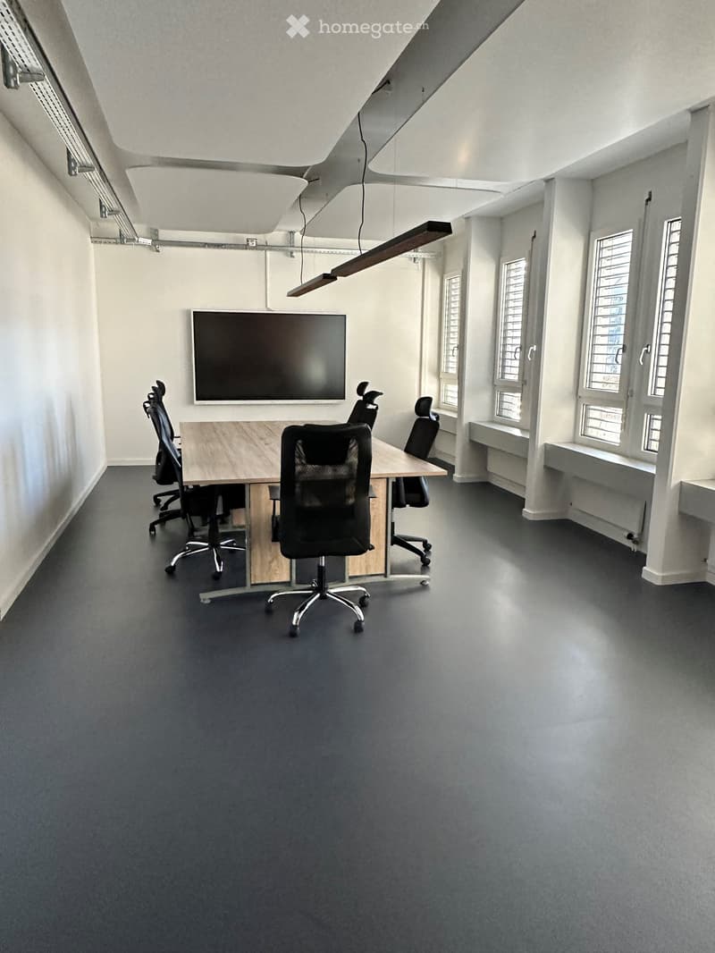 Furnished Room. Modern office space with a large screen, a wooden table, and several black office chairs.