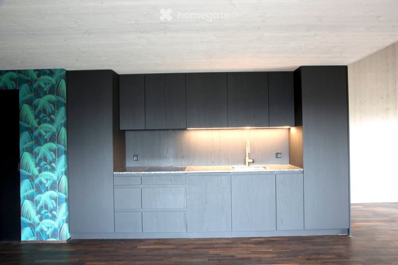 Modern kitchen with grey cabinets, a marble countertop, and a sleek faucet. The space features a wooden floor and a decorative wall with a leafy pattern.