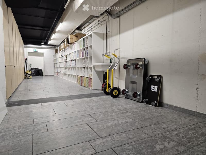 Empty hallway with tiled floor, white walls, shelves with boxes, a sink, and a small cart with wheels.