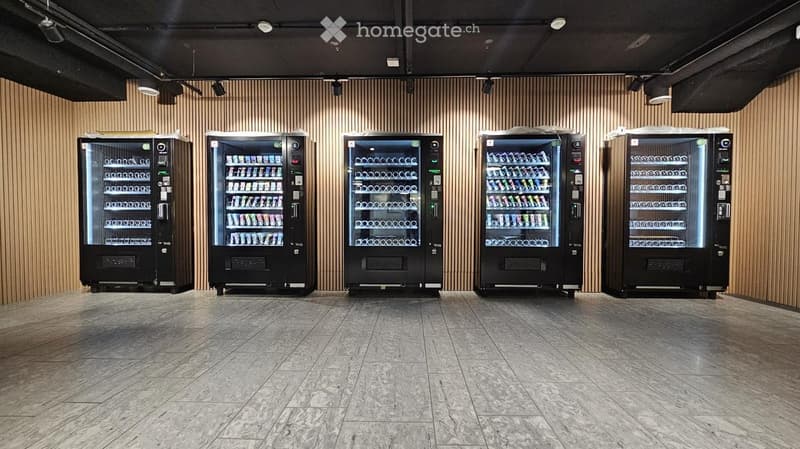 A modern, minimalist room with five black refrigerators lined up against a wooden-paneled wall. The floor is made of polished stone tiles, and the ceiling features recessed lighting.