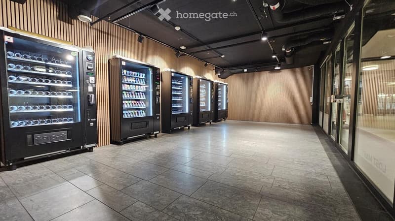 A modern hallway with several vending machines lined up against a wooden-paneled wall, featuring a polished tile floor and recessed lighting.