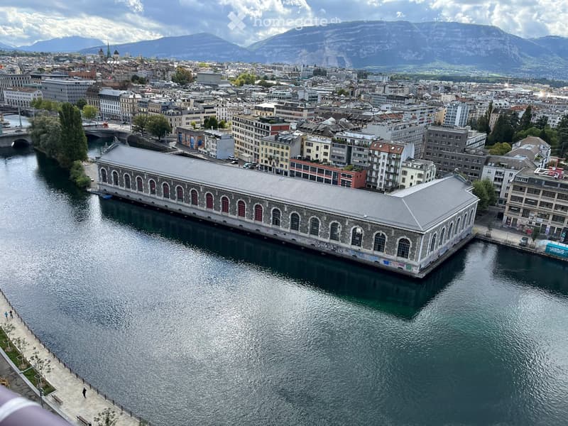 Aerial view of a cityscape with a river running through it, featuring historic buildings, modern structures, and distant mountains.
