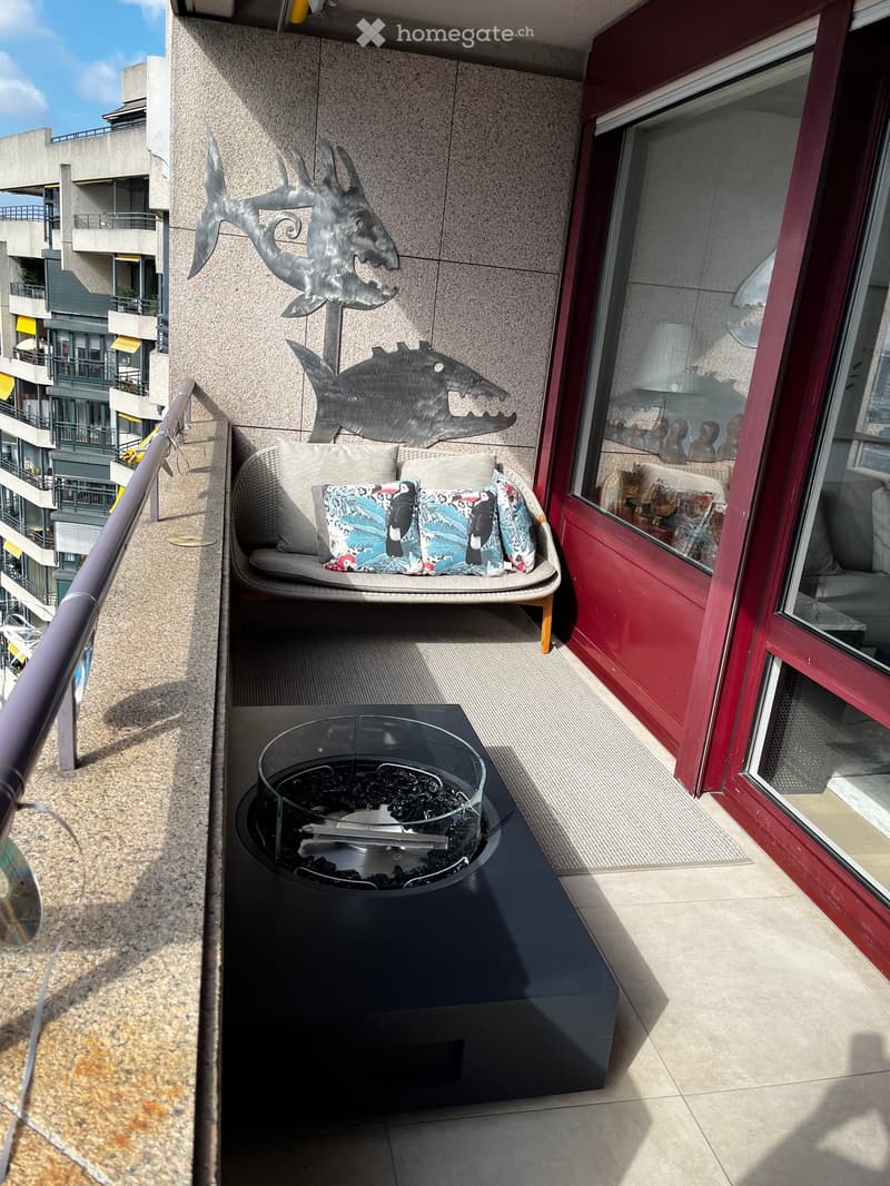 Balcony with a sofa, colorful cushions, a fire pit, and decorative metal fish sculptures on the wall.
