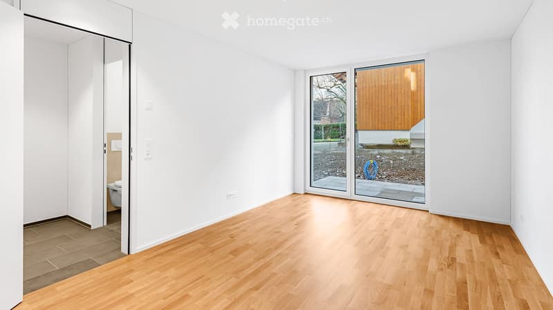Unfurnished Room. Empty room with light wooden flooring, white walls, and large sliding glass doors leading to an outdoor area. A small bathroom is visible through an open doorway on the left side.