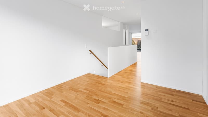 Corridor / Hallway. Bright, minimalist hallway with light wooden flooring and white walls. Features a staircase with a wooden handrail and a small built-in shelf on the wall.