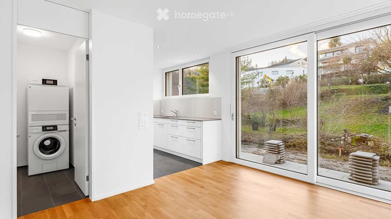 Furnished Room. Modern, well-lit room with a private washing machine, sink, and cabinets, featuring large windows and wooden flooring.