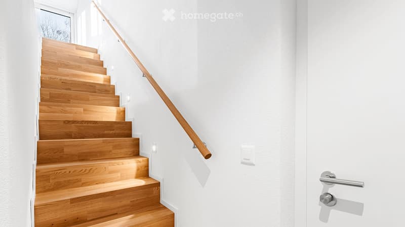 Corridor / Hallway. Modern staircase with wooden steps and a wooden handrail, white walls, and a door handle visible on the right side.