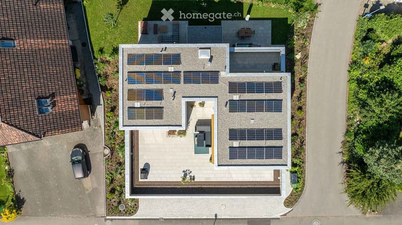 Building. A modern two-story house with a flat roof covered in solar panels, a spacious driveway, and a well-maintained garden area.