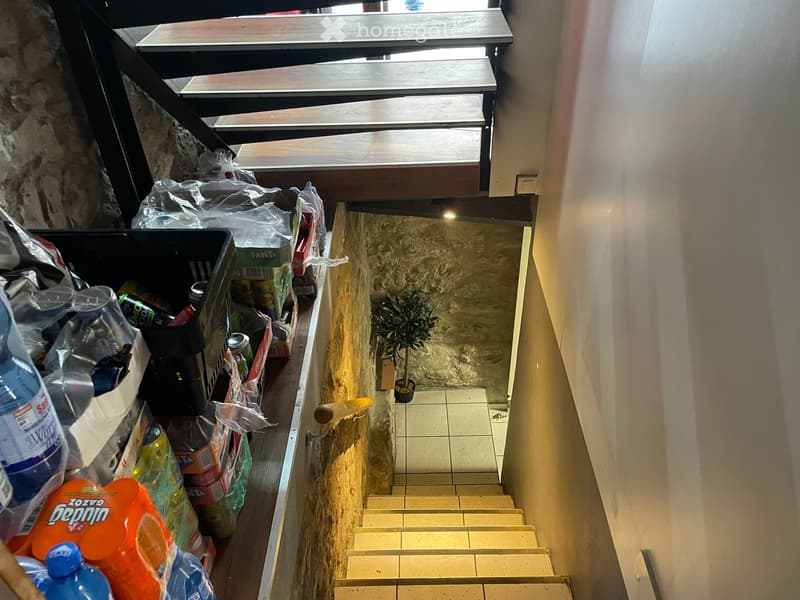 A narrow hallway with tiled steps leading upwards, a small potted plant on the landing, and a collection of trash bags and items stacked on the left side.