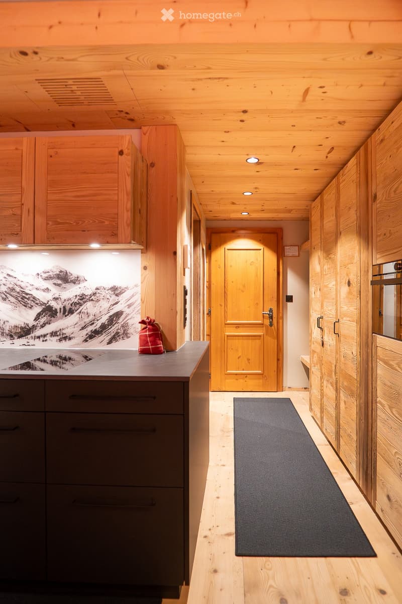 Kitchen with wooden cabinets, granite countertop, stainless steel sink, dark brown drawers, wooden ceiling, wooden floor, rug, and a door.